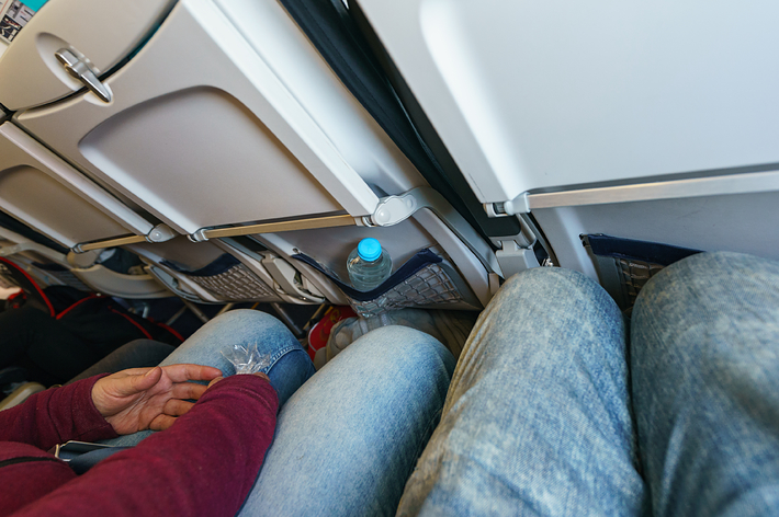飛行機の客席で並んで座る乗客たちの膝元の様子。非常に狭い空間です。