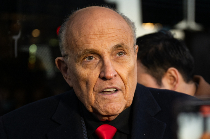 Rudy Giuliani wearing a dark suit with a red tie