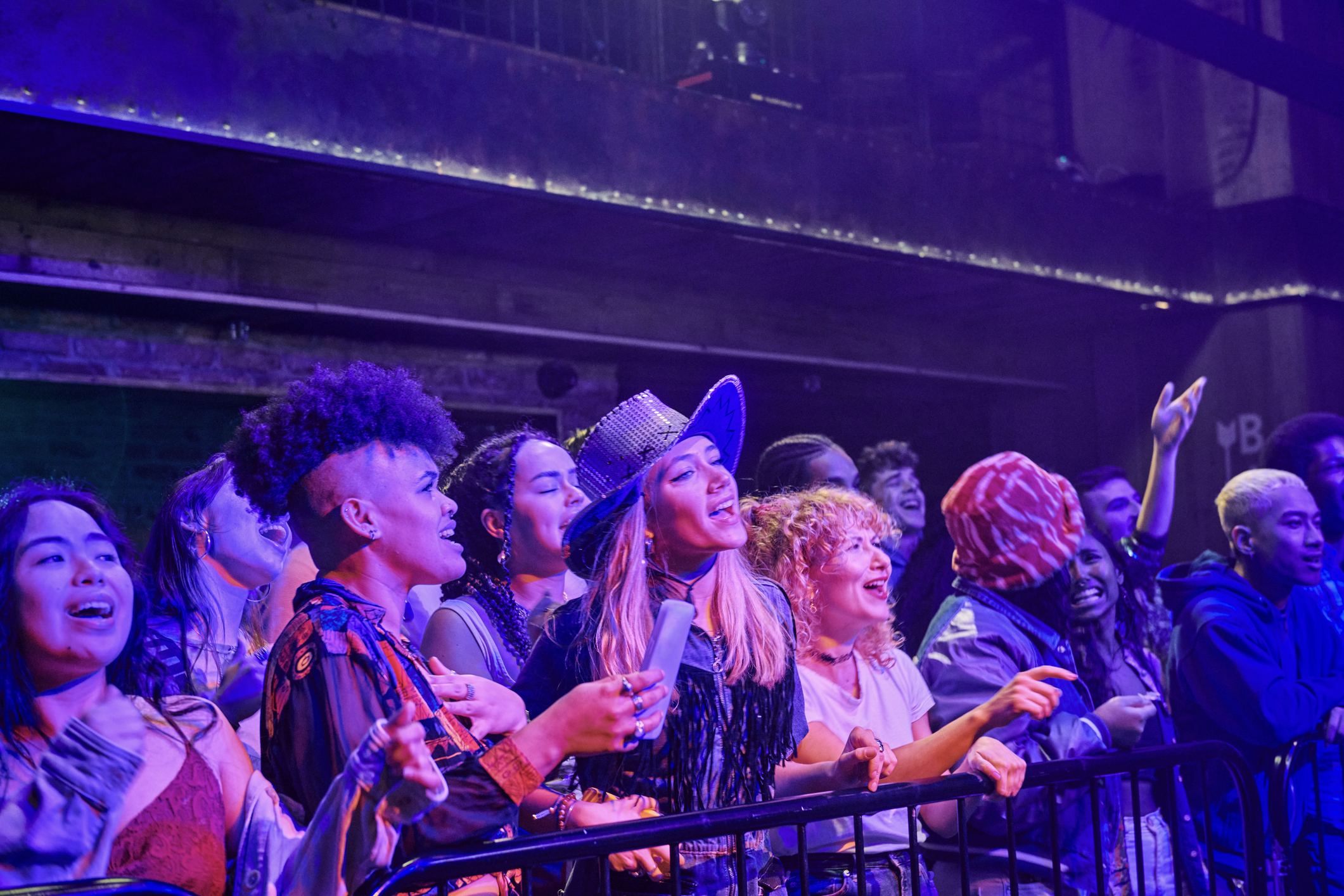 People at a concert enjoying the music enthusiastically, many wearing hats and colorful outfits