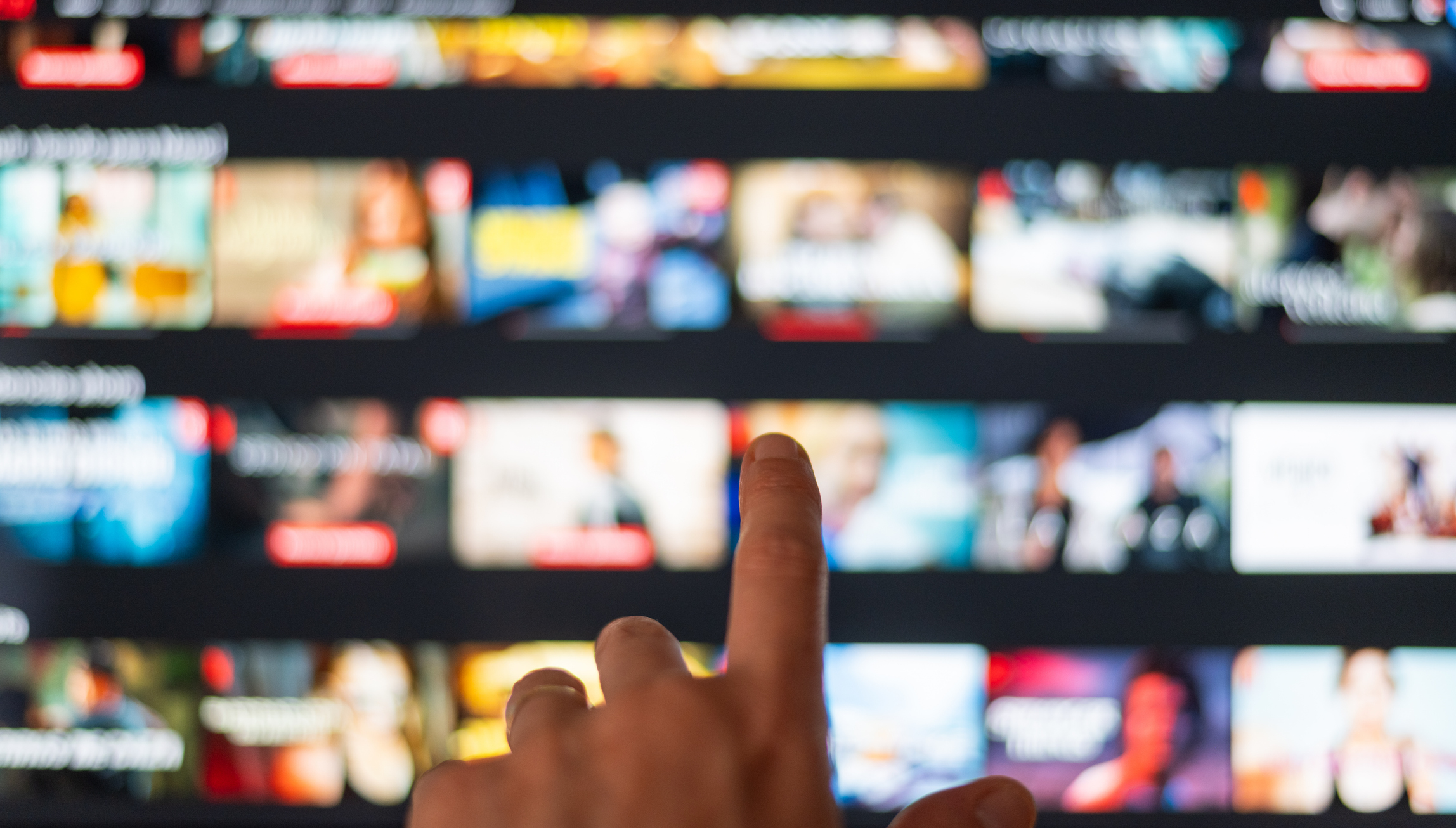 A hand is pointing at a blurred TV screen displaying various streaming options