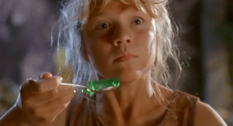 A young girl with messy hair holds a spoon with green jello
