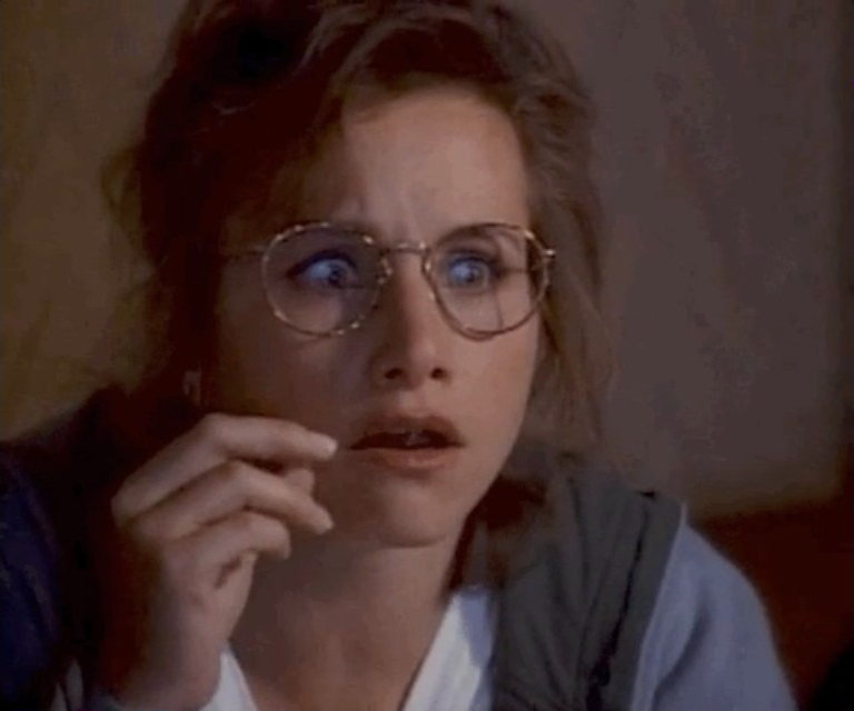 Courtney Cox looks surprised, holding a toothpick near her mouth. She is wearing glasses and a casual outfit