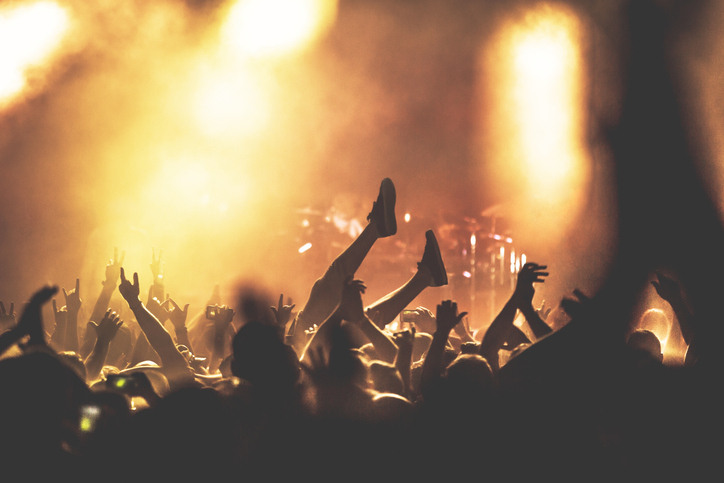 A lively concert scene with a crowd of people. A person is being carried above the crowd, presumably &quot;crowd surfing,&quot; with lots of raised hands surrounding them