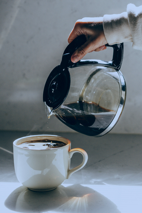 A hand pours coffee from a glass carafe into a white mug
