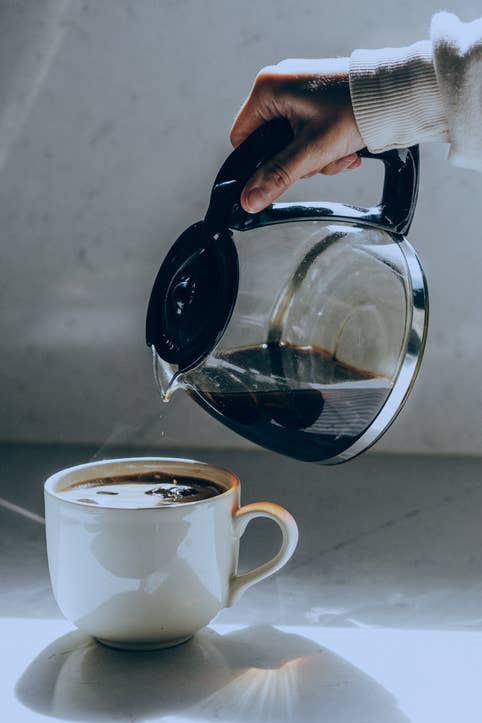 A hand pours coffee from a glass carafe into a white mug