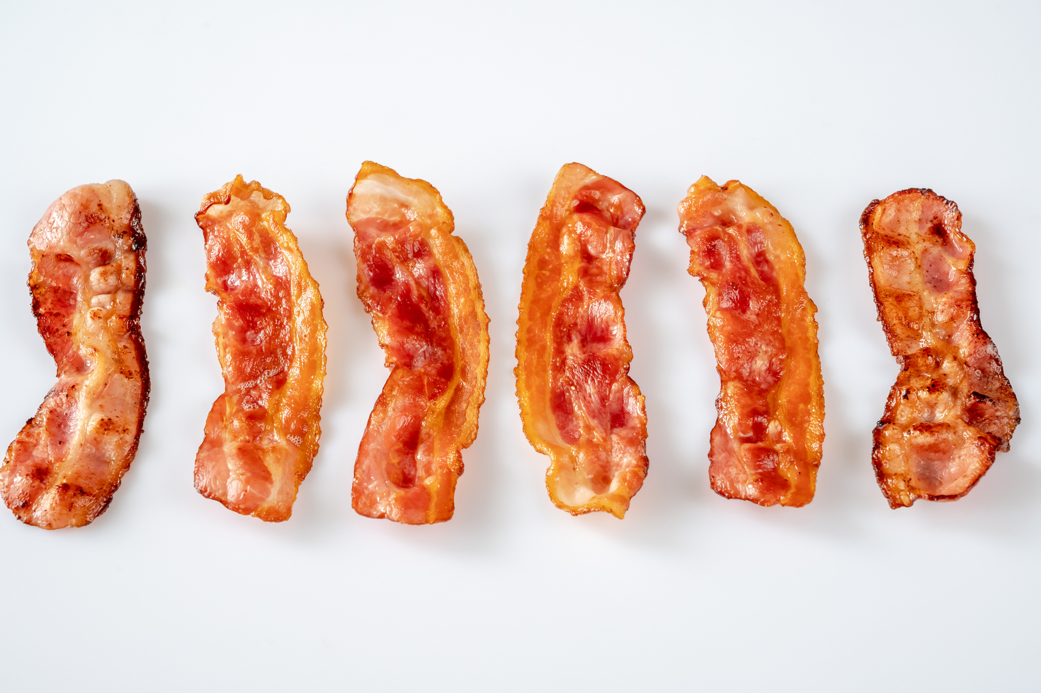 Six slices of cooked bacon arranged in a row on a white surface
