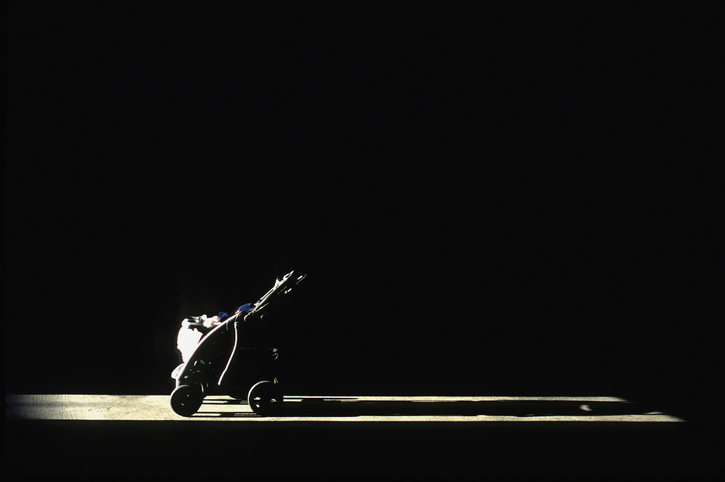 A single baby stroller is illuminated by a spotlight against a dark background. No people are present
