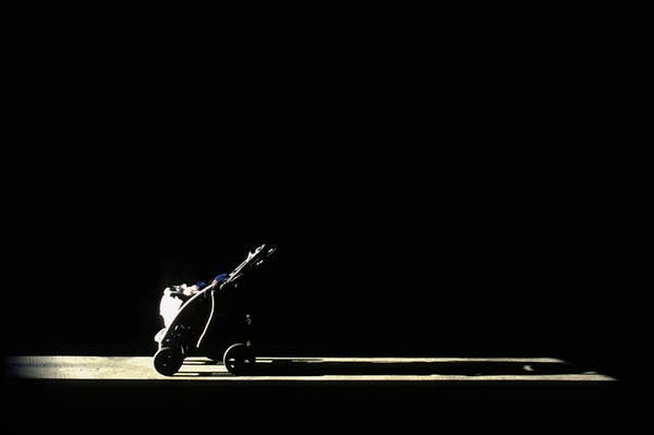 A single baby stroller is illuminated by a spotlight against a dark background. No people are present
