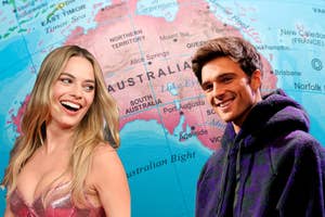 Margot Robbie in a sleeveless dress and Jacob Elordi in a casual hoodie, smiling in front of a map of Australia