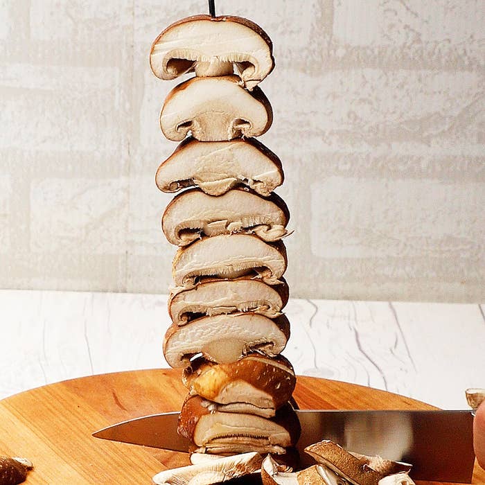 シェフのナイフが、まな板の上で重ねられたしいたけを切っている。