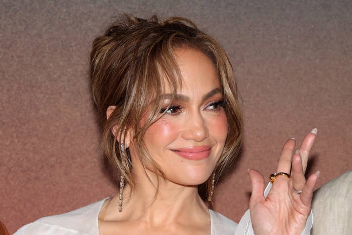 Jennifer Lopez with long earrings, smiles and waves at an event