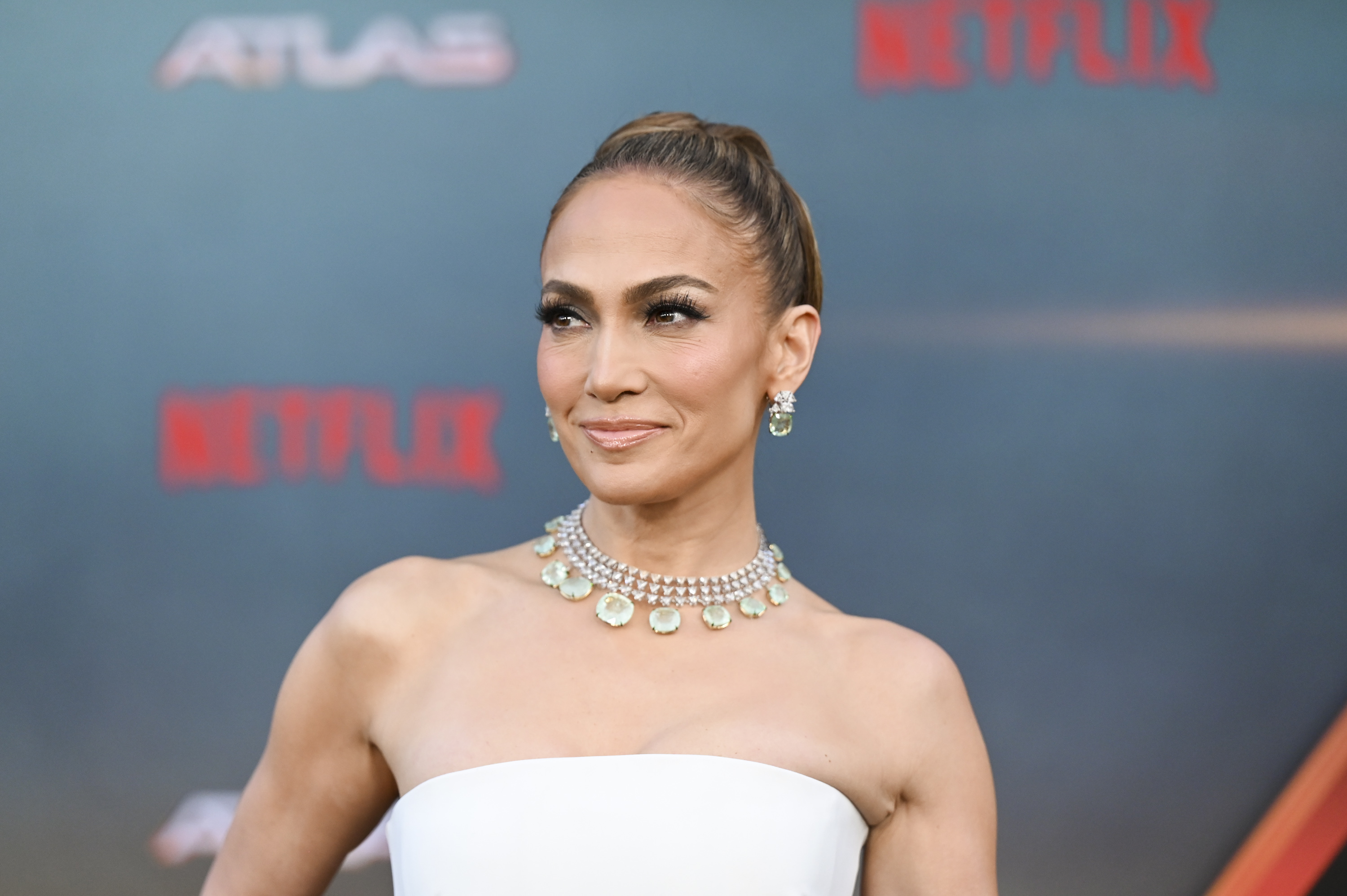 Jennifer Lopez poses on the red carpet, wearing an elegant strapless gown, statement necklace, and earrings