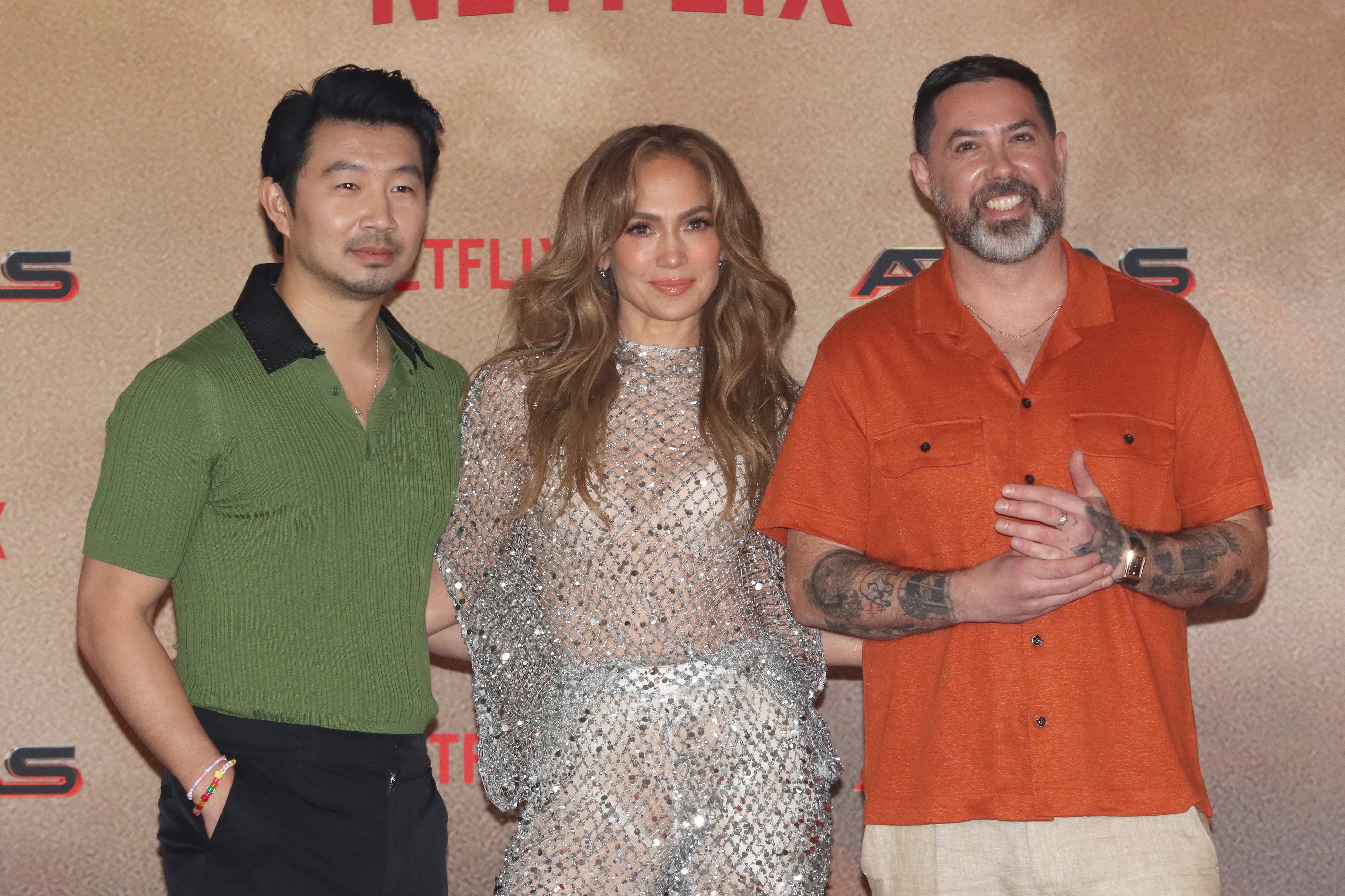 Simu Liu, Jennifer Lopez wearing a sparkling outfit, and Brad Peyton posing together at a Netflix event