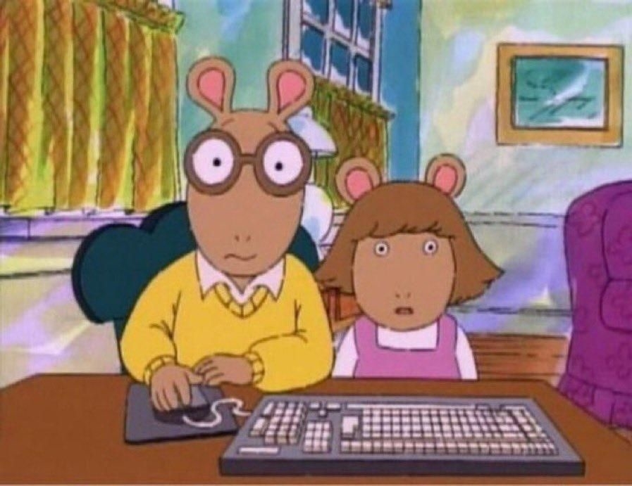 Arthur and D.W. from the animated series "Arthur" sit at a computer, looking surprised. Arthur is using the mouse while D.W. watches