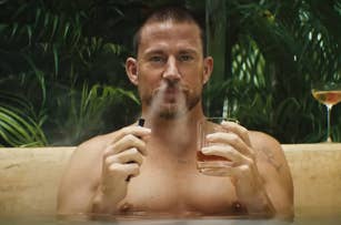 Channing Tatum sits shirtless in a hot tub, holding a vape pen in one hand and a glass of whiskey in the other, with greenery in the background