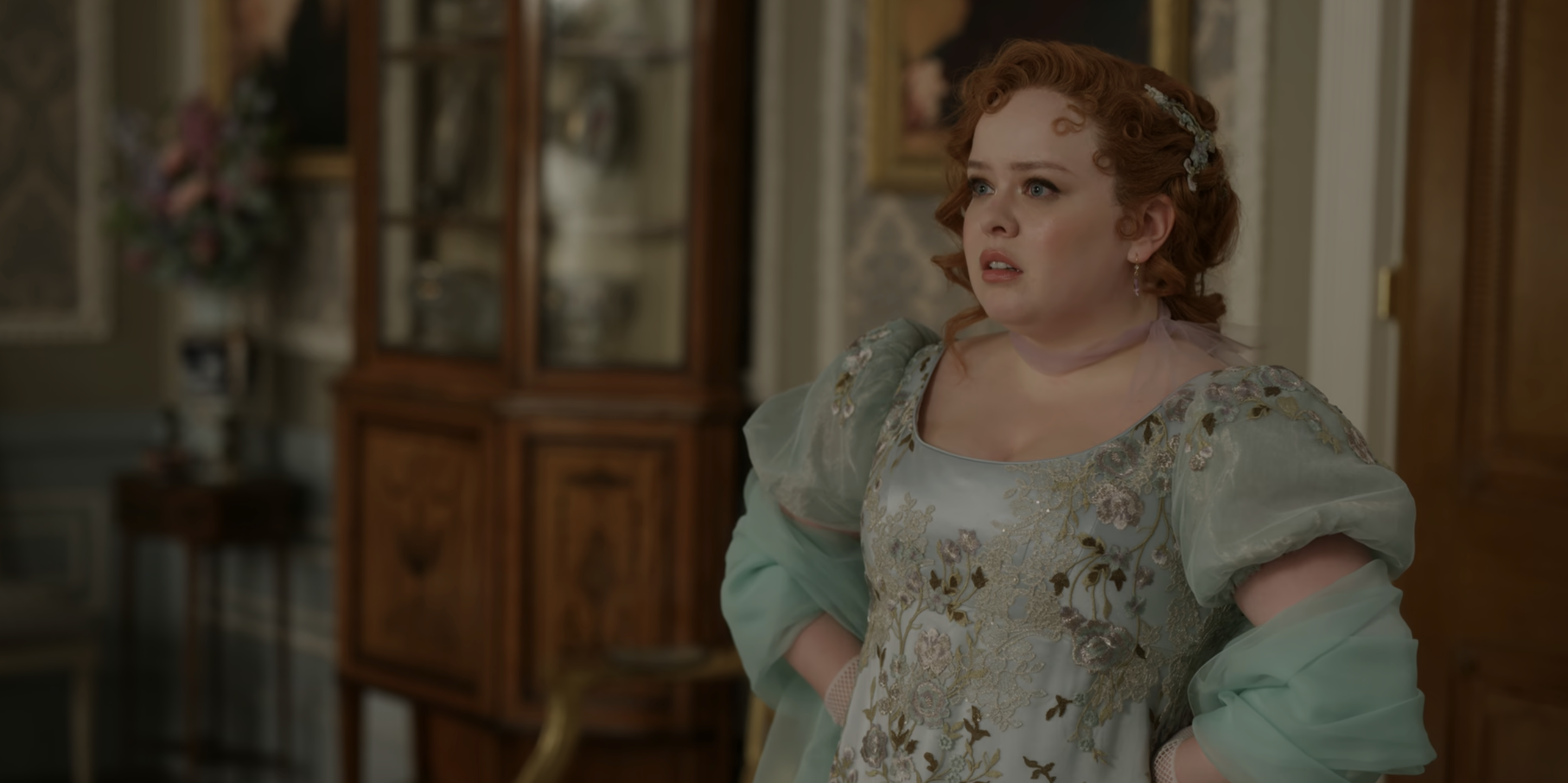 Penelope in a period costume with floral embroidery, styled hair, and an anxious expression, standing in an opulent room