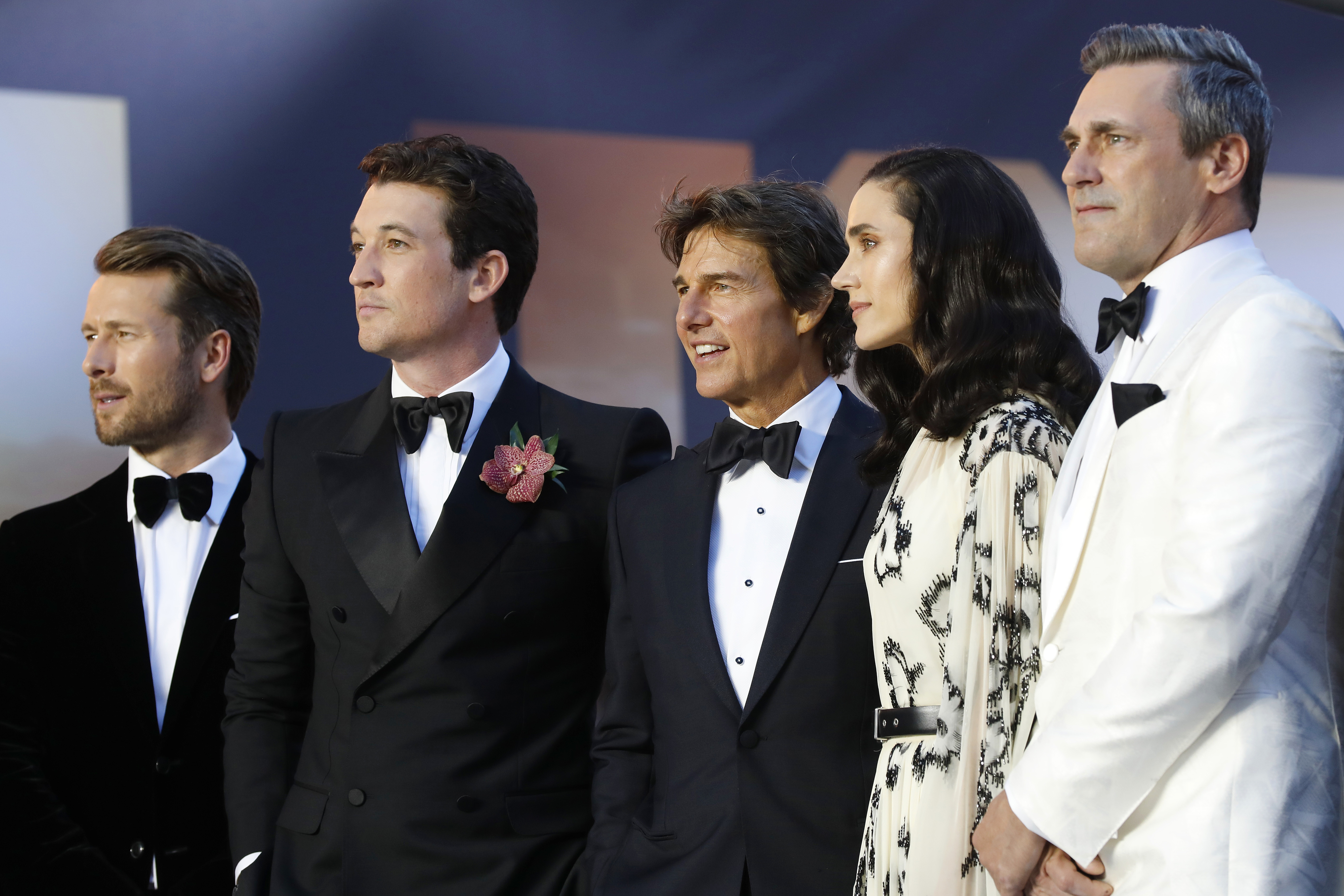 Glen Powell, Miles Teller, Tom Cruise, Jennifer Connelly, and Jon Hamm stand together on the red carpet, dressed in formal attire