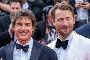 Tom Cruise and Glen Powell smile on the red carpet wearing tuxedos with bow ties. Photographers are visible in the background