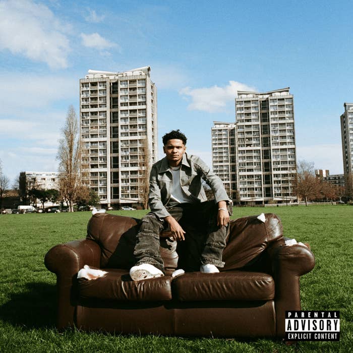 Music artist Roddy Ricch sits on a brown couch in a grassy field with tall apartment buildings in the background. Parental Advisory label in the bottom right