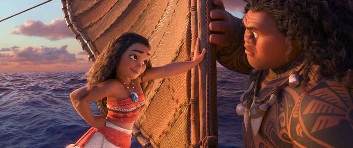 Moana and Maui sail on a boat, exchanging determined looks. Moana wears a traditional Polynesian outfit; Maui has tattoos covering his arm and chest