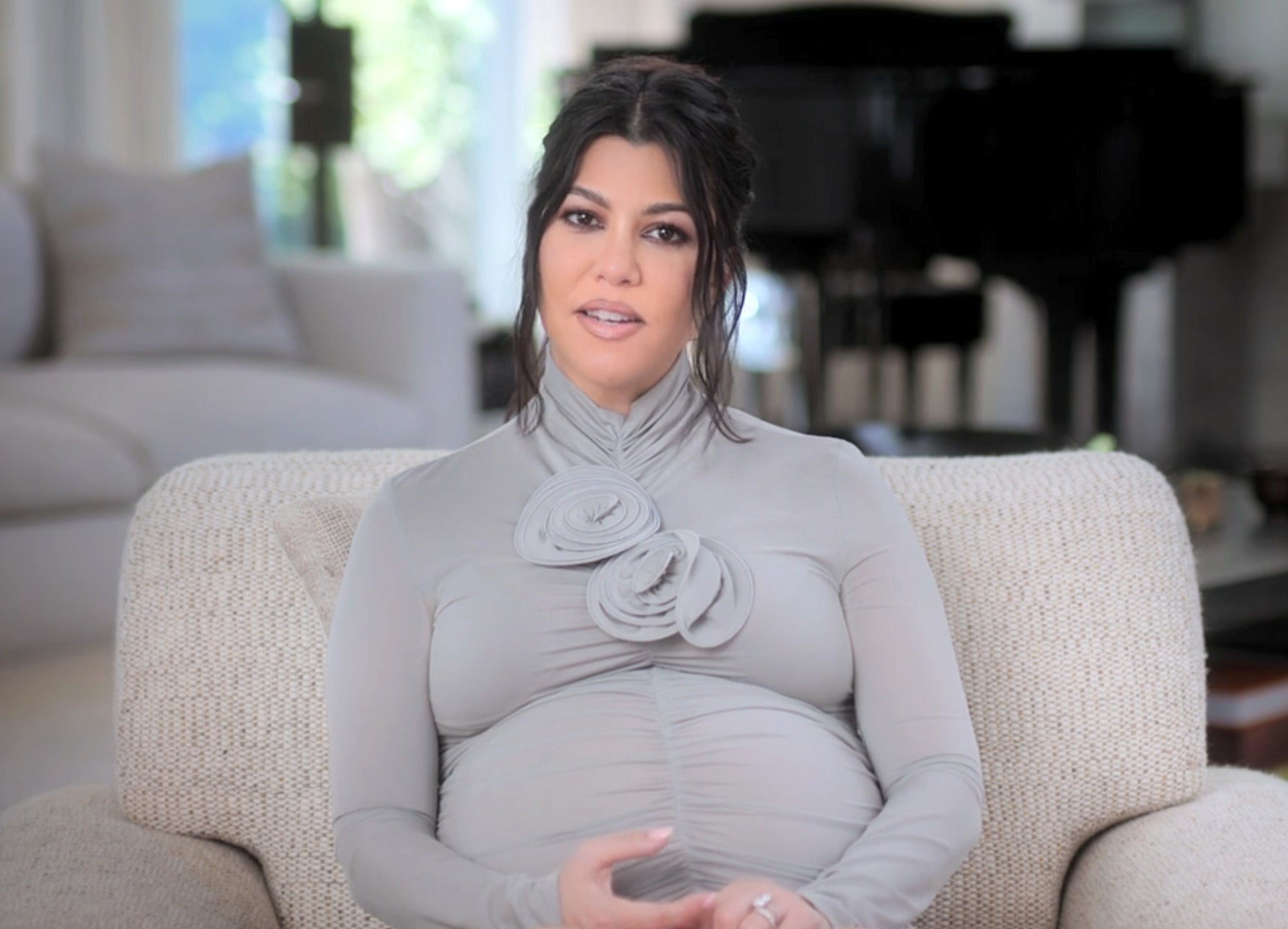 A pregnant Kourtney Kardashian sits on a couch in a living room setting