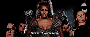 Tina Turner stands in a post-apocalyptic costume with other characters. The caption reads, "This is Thunderdome."