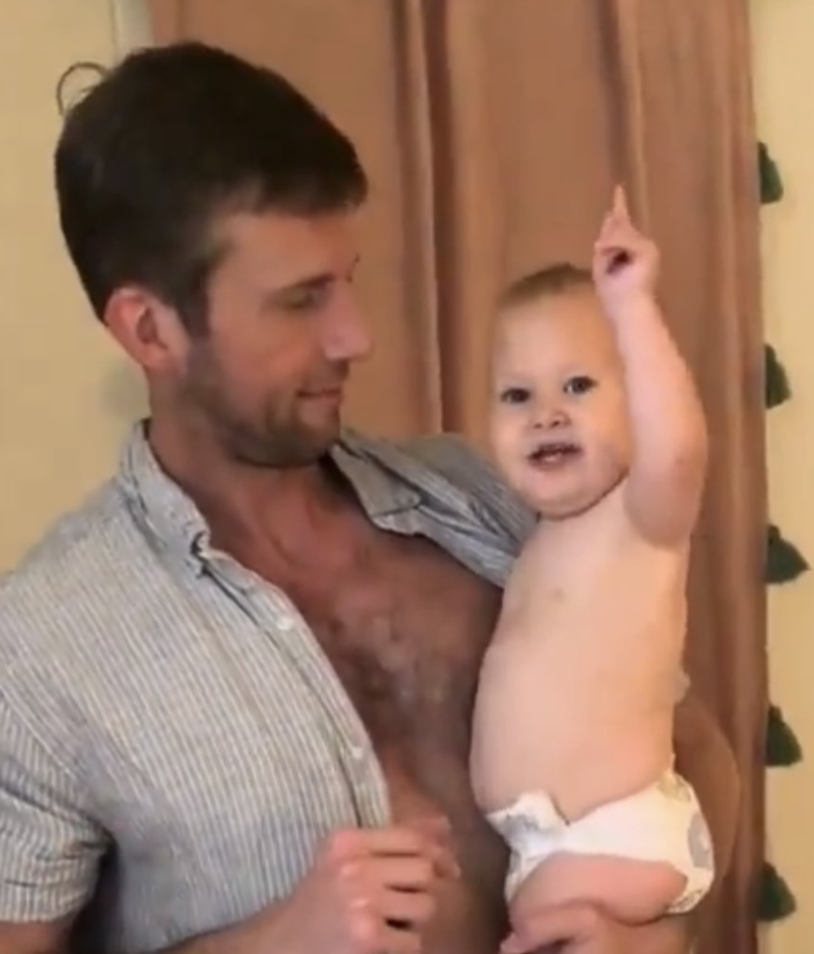 A man holding a baby who is smiling and pointing upward. The man is wearing a striped shirt