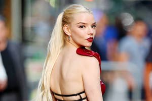 Anya Taylor-Joy, wearing a strappy red dress, poses on a red carpet with her hair in a long ponytail