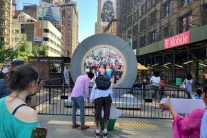 People interacting with a large, circular public art installation in an urban area with construction and storefronts in the background