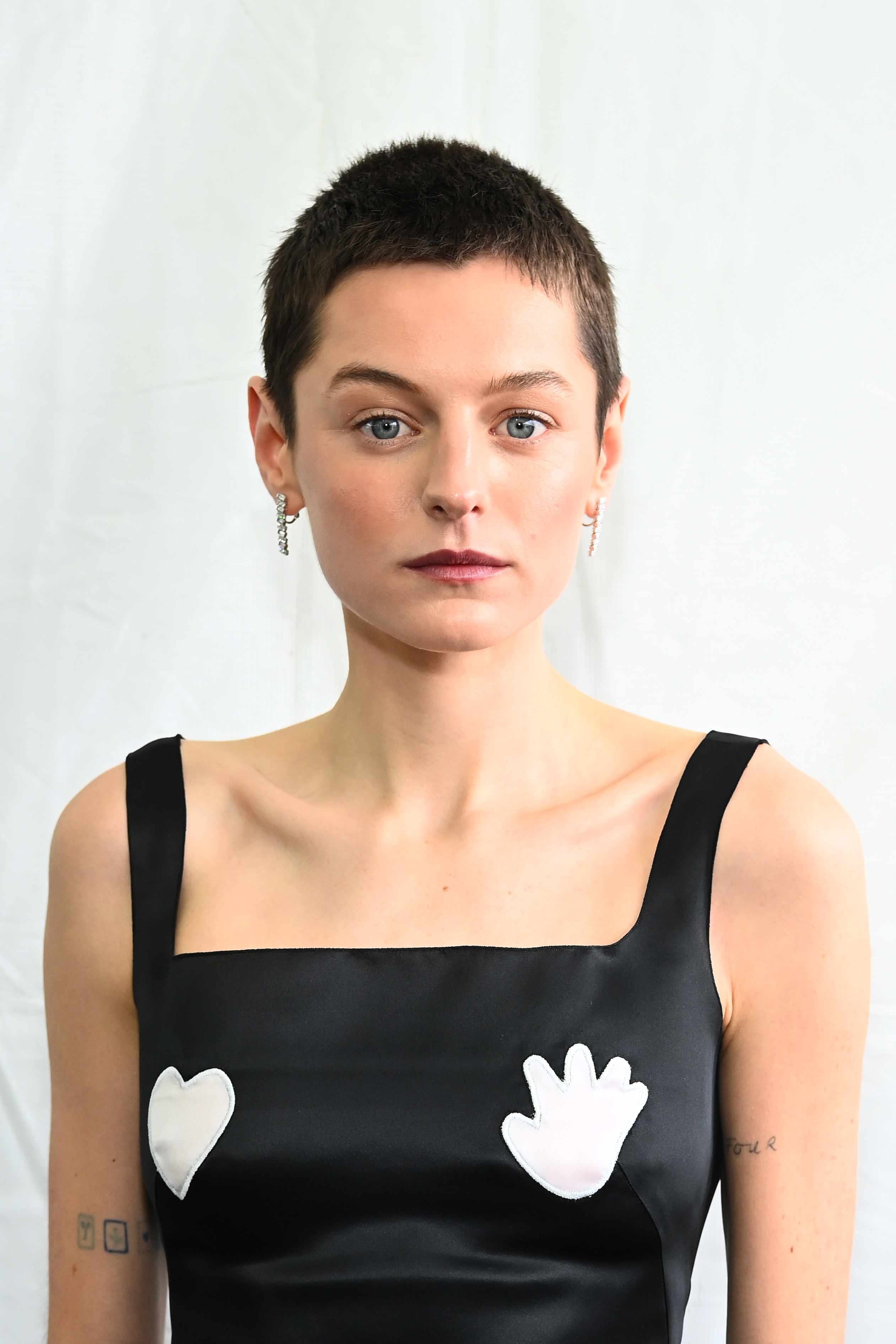 Emma Corrin wearing a minimalist black dress with white heart and hand shapes in front of a white background