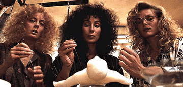 Susan Sarandon, Cher, and Michelle Pfeiffer in a scene from the film "The Witches of Eastwick," focusing intently on a white figure.