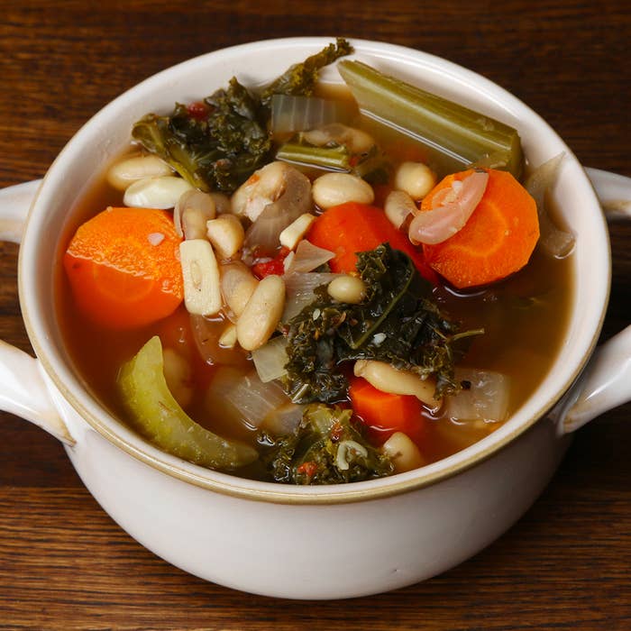 A bowl of vegetable soup containing carrots, beans, celery, kale, onions, and mushrooms