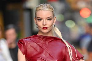 Anya Taylor-Joy poses for a photo wearing a stylish, sleeveless, textured red dress with a high neckline and unique wrap detail. Her hair is pulled back