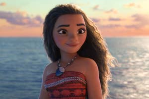Moana stands by the ocean at sunset, wearing a patterned red sarong and a necklace with a large blue pendant