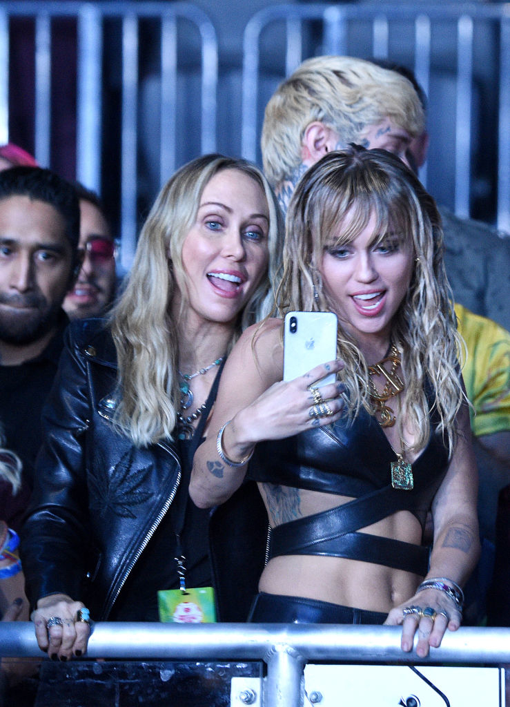 Miley Cyrus takes a selfie with her mother Tish Cyrus, at a public event. Miley wears aleather outfit, and both are smiling