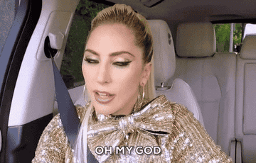 Lady Gaga in a car, expressing surprise with the text "OH MY GOD" at the bottom. She is wearing a sparkling outfit with a large bow