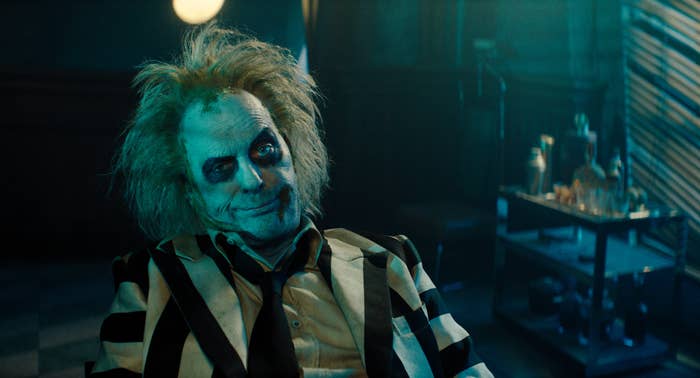Character Beetlejuice from the movie &quot;Beetlejuice&quot; smirking, wearing a black and white striped suit, messy hair, and dark eye makeup