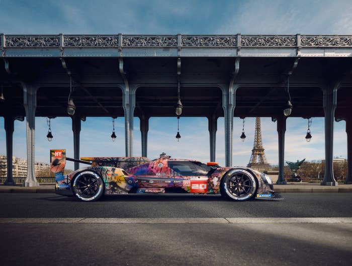 Art car with colorful graffiti design featuring animated characters, parked under a bridge in Paris with the Eiffel Tower visible in the background