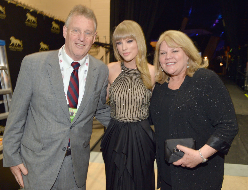 Taylor Swift in a sleeveless, high-neck gown and her parents posing together at an event