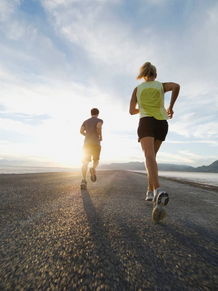 Two people running on a road towards the horizon with the sun setting in the background