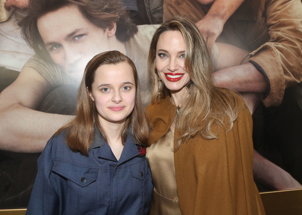 Vivienne Jolie-Pitt and Angelina Jolie pose together at a public event. Vivienne is wearing a acket, and Angelina is in a dress with a shawl