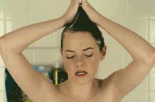 Woman in a shower with hands on her head, eyes closed, looks relaxed