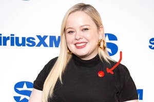 Nicola Coughlan smiles while wearing a black top and large hoop earrings at a SiriusXM event. 

