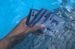 A hand holds several waterproof playing cards submerged in a swimming pool, featuring the 4 of hearts and 2 of diamonds