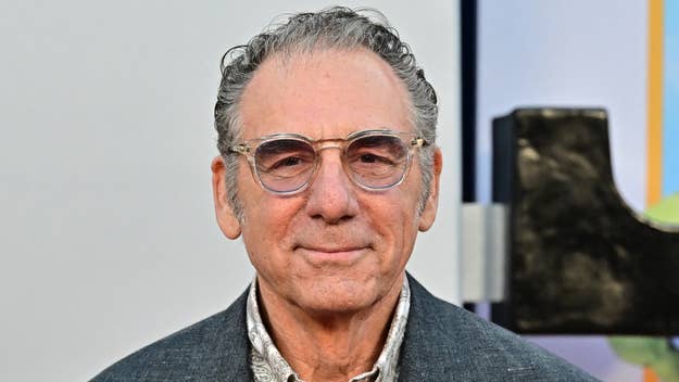 Michael Richards at an event, dressed in a tailored suit with a patterned shirt and clear glasses