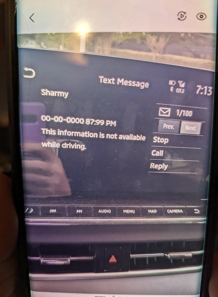 Car dashboard screen displaying a text message from "Sharmy" that reads "This information is not available while driving." Time displayed is 7:13 PM