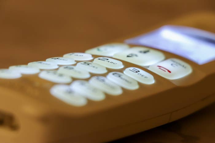 Close-up of a landline telephone handset with buttons and a screen lit up