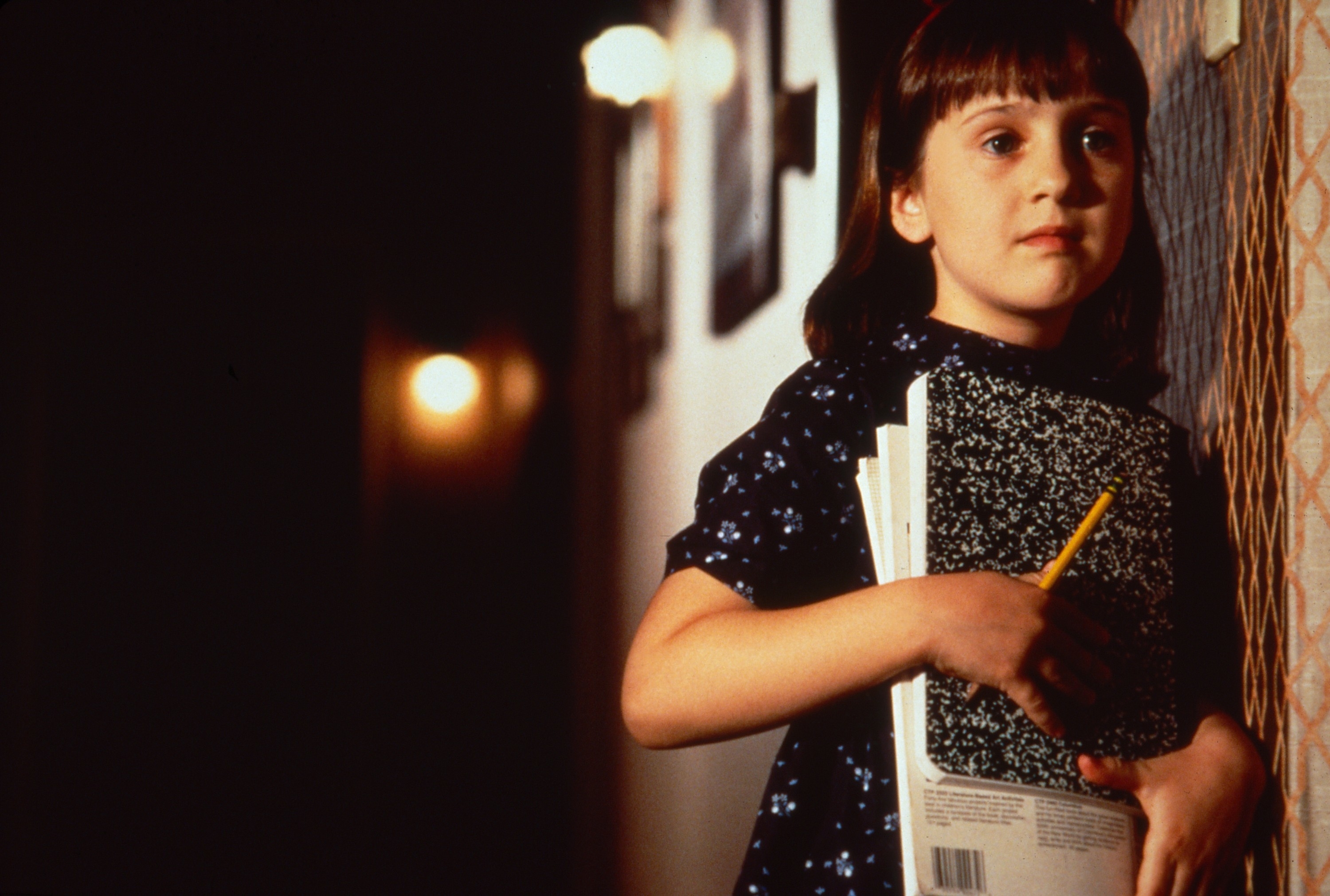 Mara Wilson as Matilda holding school supplies while wearing a floral dress