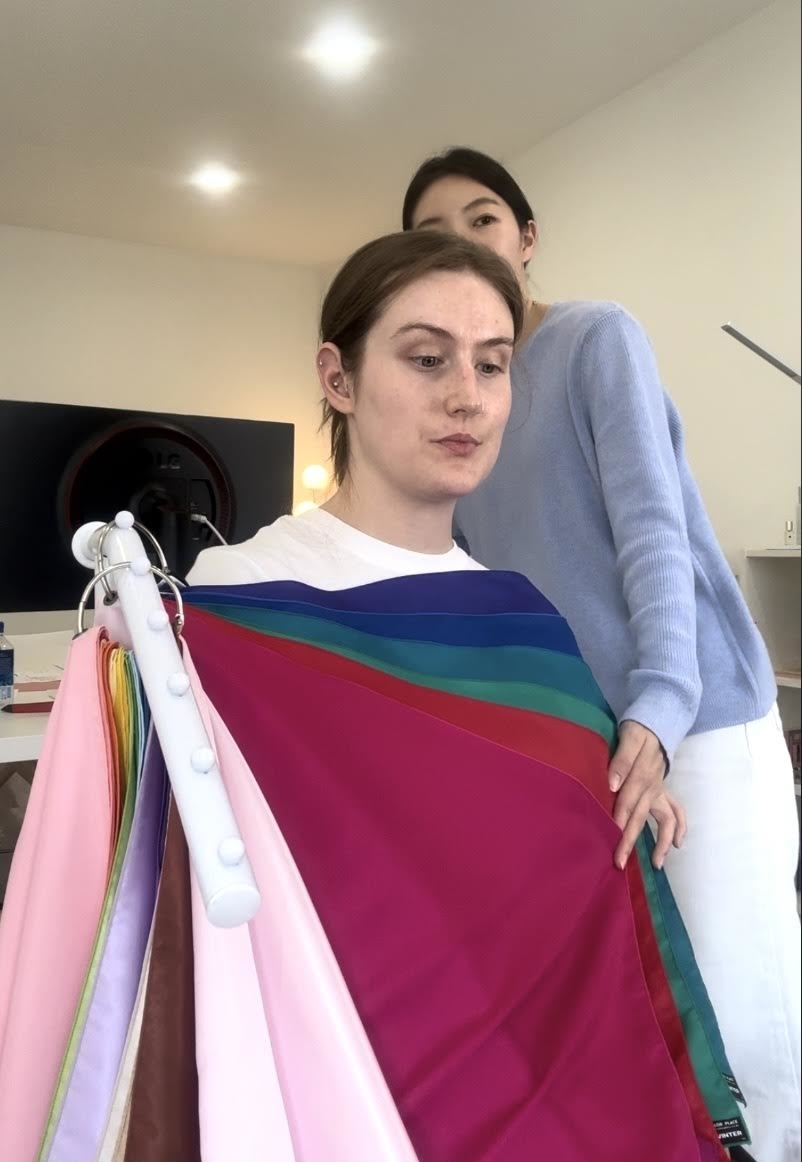 Two people holding a color analysis drape fan with various fabric swatches