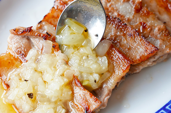 玉ねぎをのせた焼いた肉のクローズアップ画像。スプーンで玉ねぎを盛り付けています。